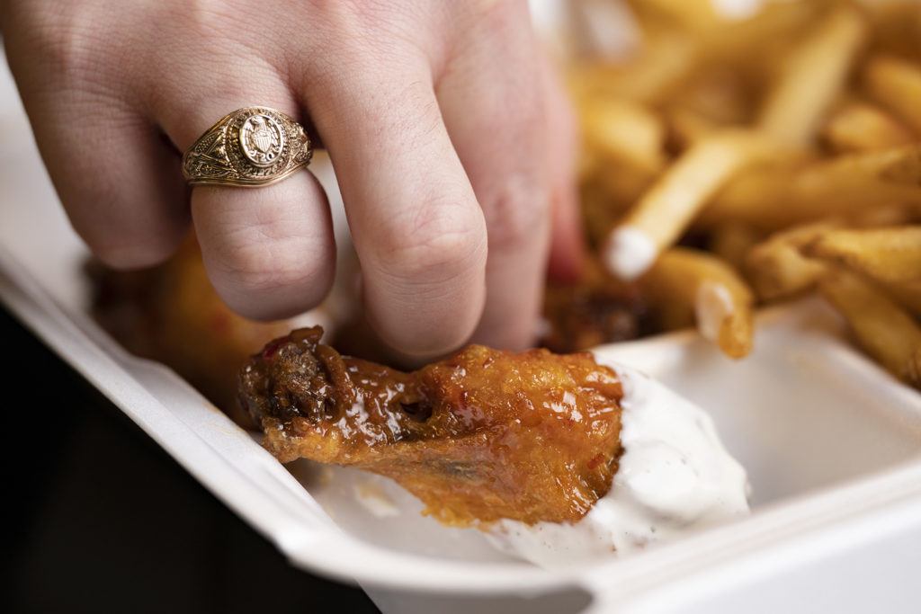 hand wearing aggie ring dunking a chicken wing into ranch dressing