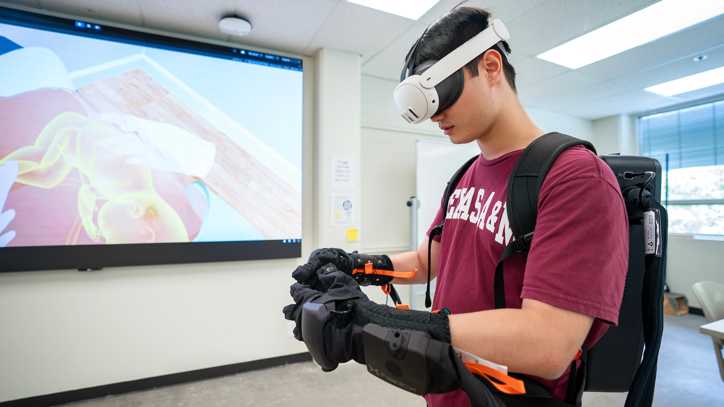A Texas A&M student wearing a VR headset and connected gloves interacts with a virtual baby