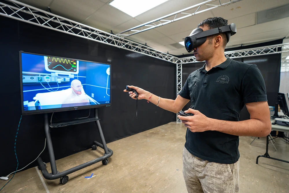 A student wearing a VR headset interacts with a virtual patient in a hospital room