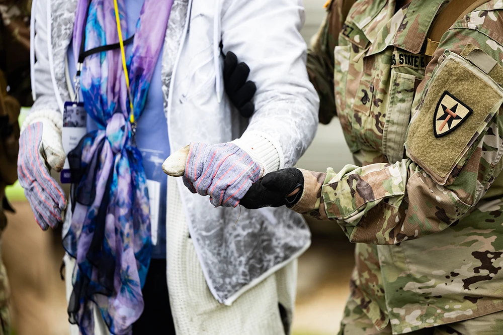 Person in combat fatigues holds the gloved hand of an older woman