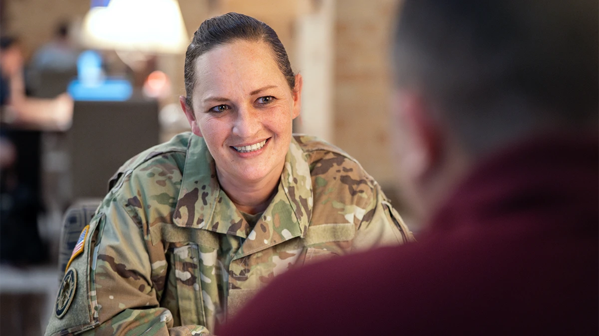 Woman in military fatigues speaks to a person in a maroon polo